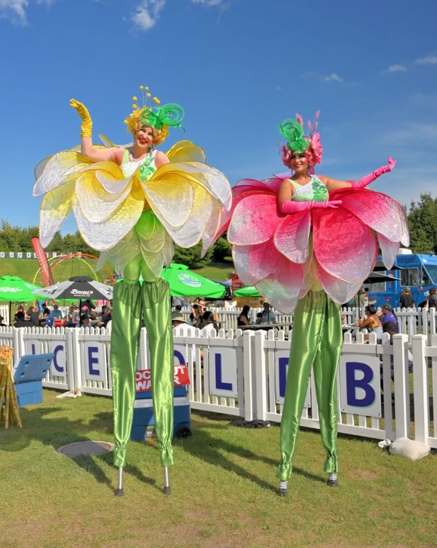 Two flower stilt-walkers in yellow and pink petal costumes at outdoor festival